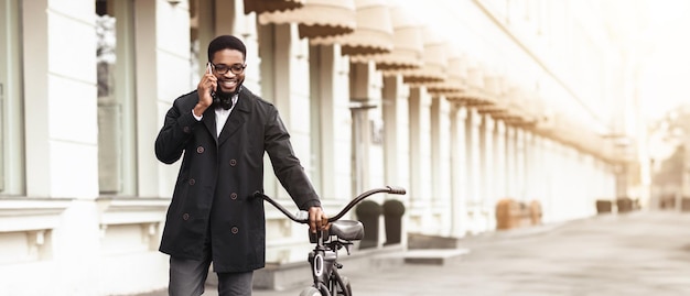 Black businessman is sitting on his bicycle using his phone outdoors the atmosphere is relaxed and