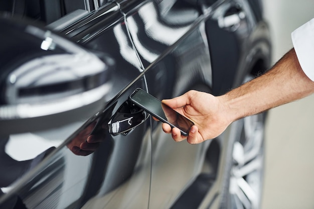 Black car Close up view of man's hand that holds phone with labels and icons Conception of remote control