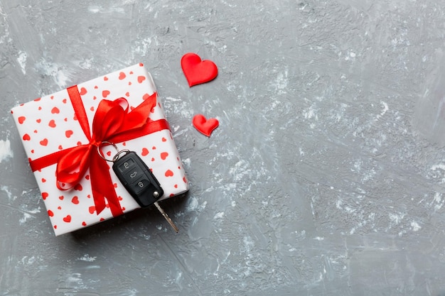 Black car key in a present box with a ribbon and red heart on colored background Valentine day composition Top view