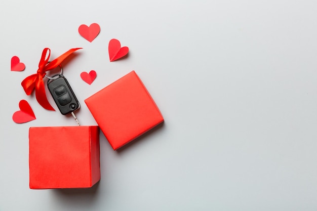 Black car key in a present box with a ribbon and red heart on colored background Valentine day composition Top view