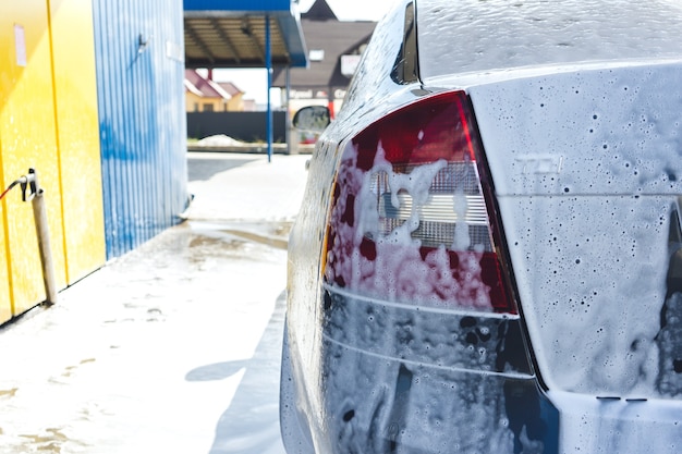 Black car in white foam on a manual car wash. Gray car washed in white foam. Car at the car wash.