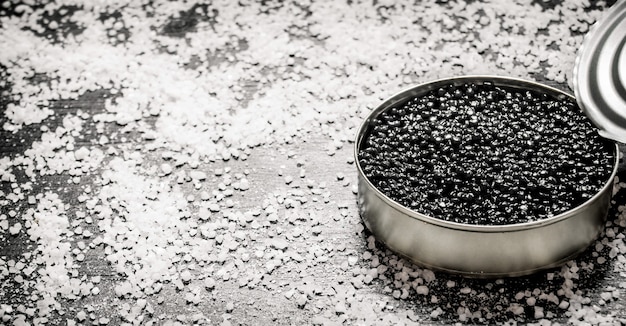 Black caviar in a jar with salt . On a black wooden table. Free space for text .