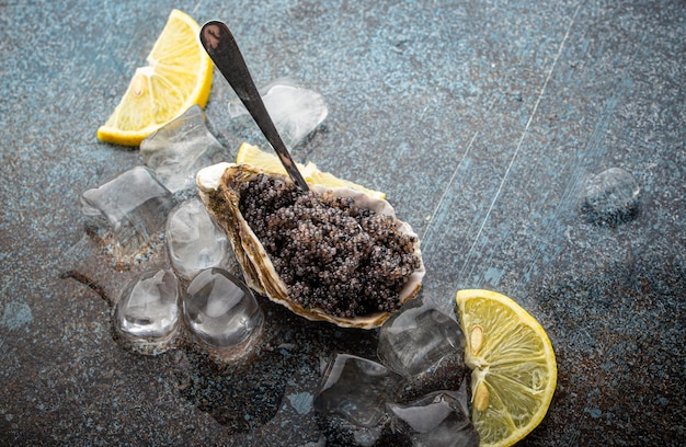 Black caviar served in oyster shell with spoon with lemon wedges and ice cubes