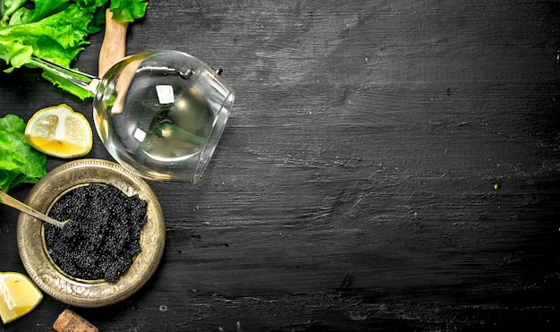 Black caviar with white wine and herbs. On a black chalkboard.