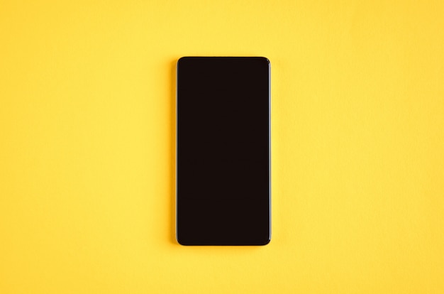 Black cellphone on yellow surface, mobile phone.