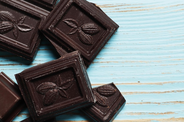 Black chocolate different pieces and a bar on a blue wooden background. Top view. Place for text.