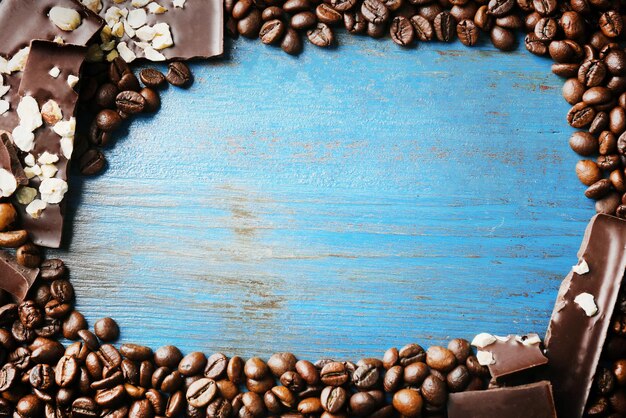 Black chocolate pieces with nuts and coffee grains on color wooden background