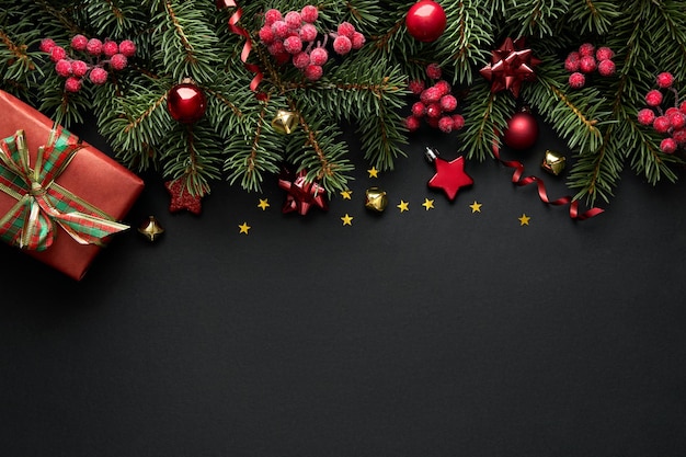 Black Christmas background with Christmas tree branches and red berries, winter festive composition with copy space. Top view.