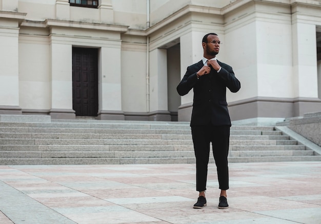 Black-clad black man settles his tie out in town.