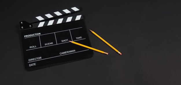 Black clapper board or movie slate with 2 pencils isolated on black background