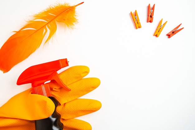 Black cleansing spray in hand in orange glove, clothespins and orange feather on white table