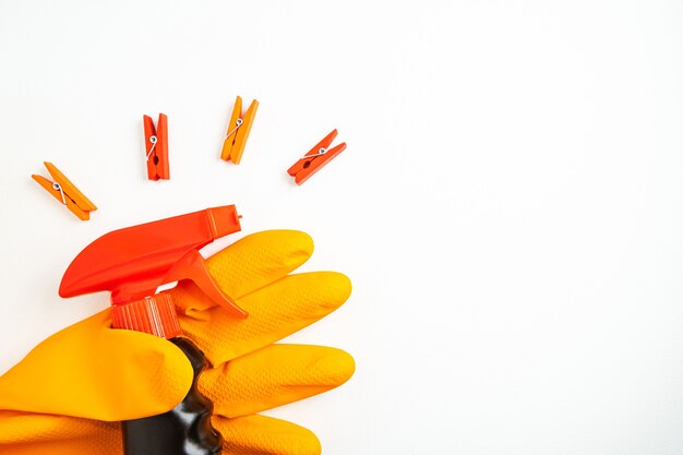 Black cleansing spray in hand in orange glove and multicolored clothespins on white background. Cleaning, cleanliness and household chemicals concept. Copy space