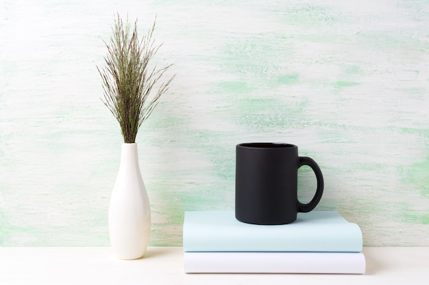 Black coffee mug  with dark meadow grass in vase and books