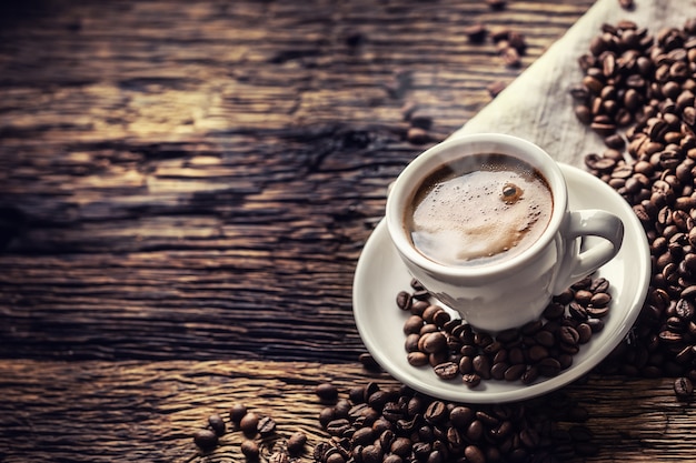 Black coffee in porcelain cup with scattered beans on rustic wooden table.