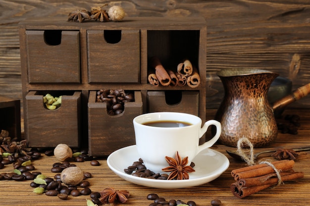 Black coffee in a white cup and spices on a wooden table