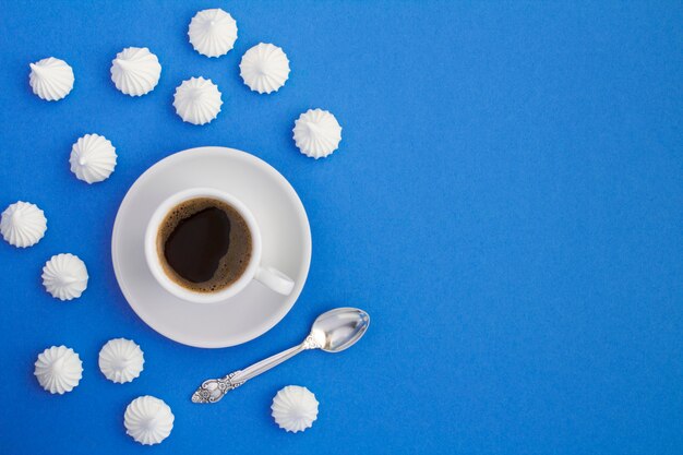 Photo black coffee in the white cup  and white meringue on the blue surface. top view. copy space.