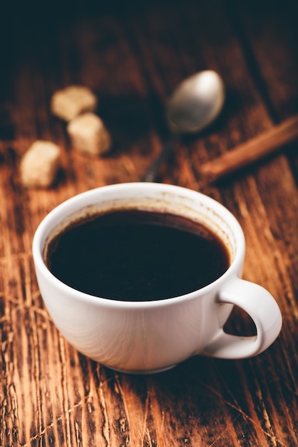 Black coffee in white cup with sugar and cinnamon sticks