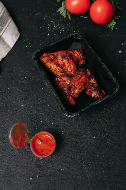 A black container with chicken wings on it sits on a black table.