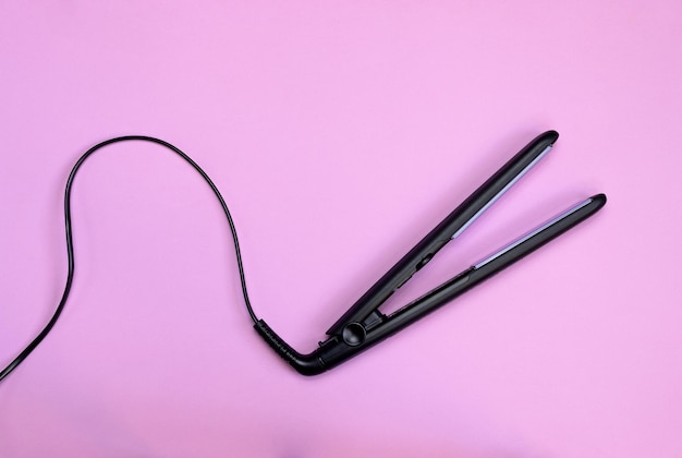 Black corded hair straightener isolated on pink background