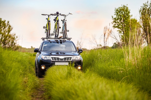 Black crossover with three bicycles on roof rack in a meadow