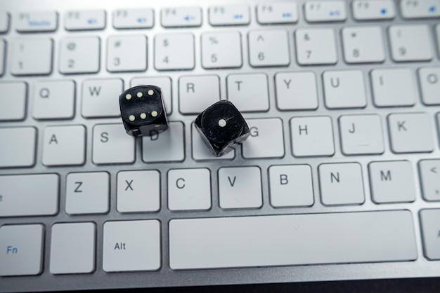 Black cubes on a white keyboard of a new laptop isolated on a black table View from above Online gambling and casino concept dice close up