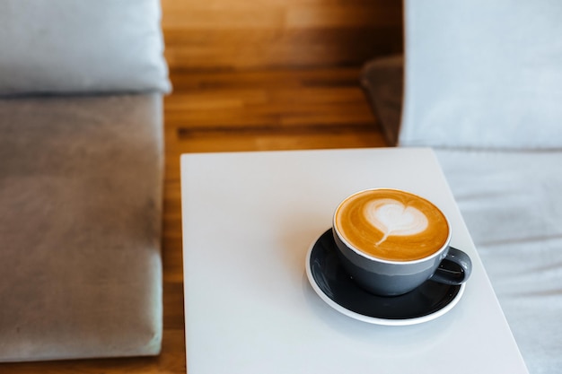 Black cup of cappuccino on saucer with latte art on white table background