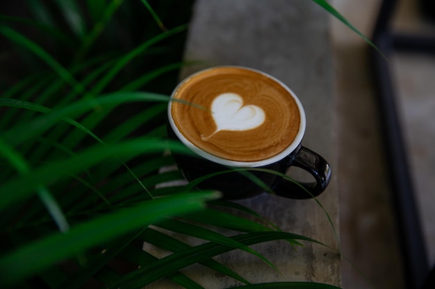 Black cup of cappuccino with latte art of heart shape on saucer on concrete background