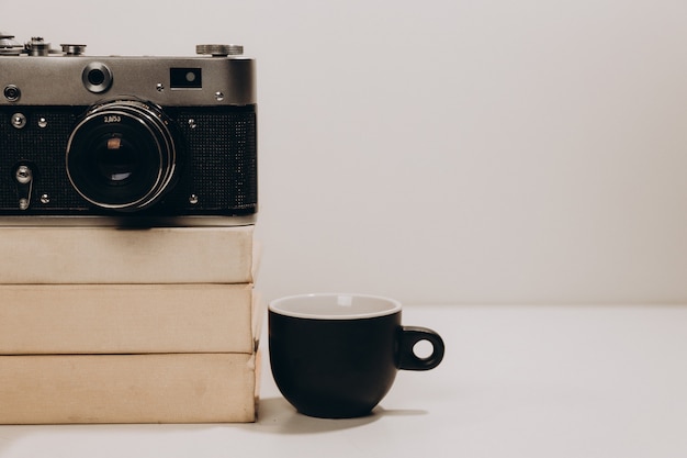 Black cup of coffee with old vintage camera and white books