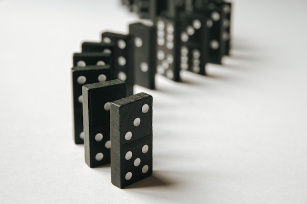 Black dominoes chain on a white table background Domino effect concept