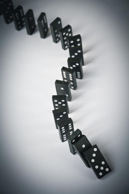 Black dominoes chain on a white table background Domino effect concept