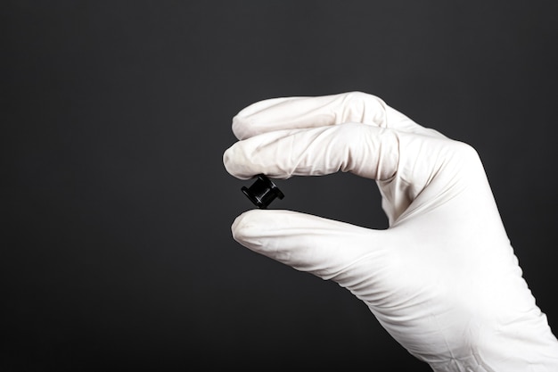 Black ear tunnel in hand with white disposable glove on dark background close-up, piercing, ear jewelry.