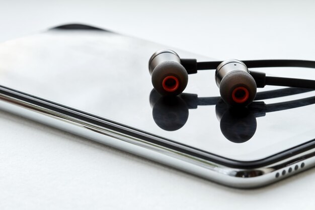 Photo black earphones lie on the modern smartphone. white background, closeup