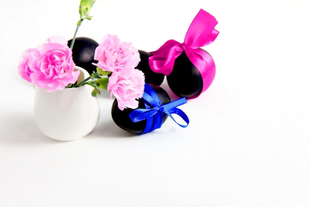 black easter eggs and pink carnation flowers on a white background