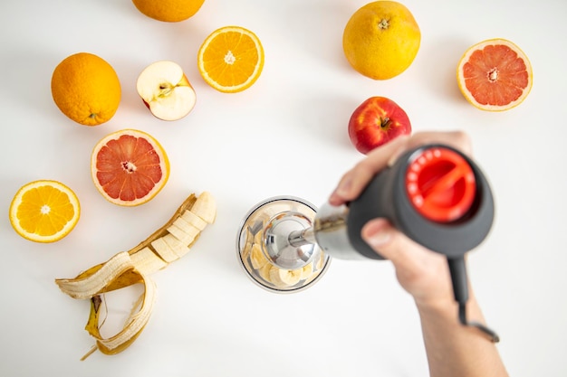 Black electric hand blender and accessories with sliced fruits on a white background Top view flat lay