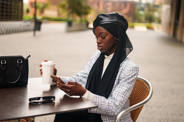 Black elegant woman drinking coffee and browsing smartphone