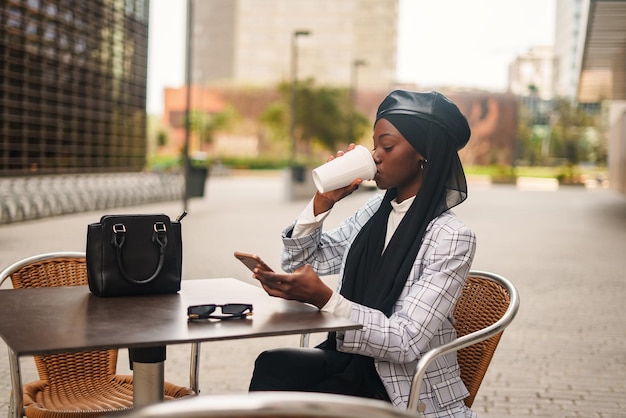 Black elegant woman drinking coffee and browsing smartphone