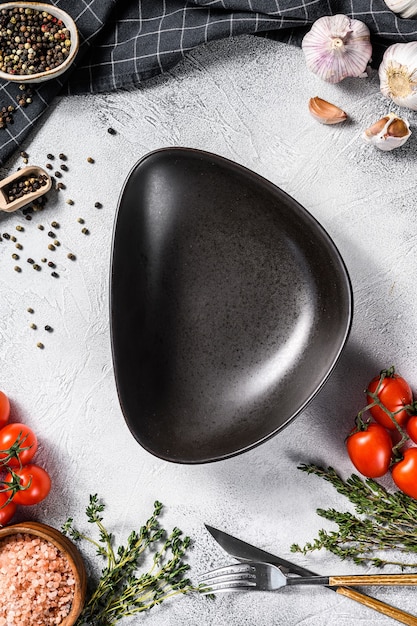 Black empty plate in center of Fresh raw greens, vegetables