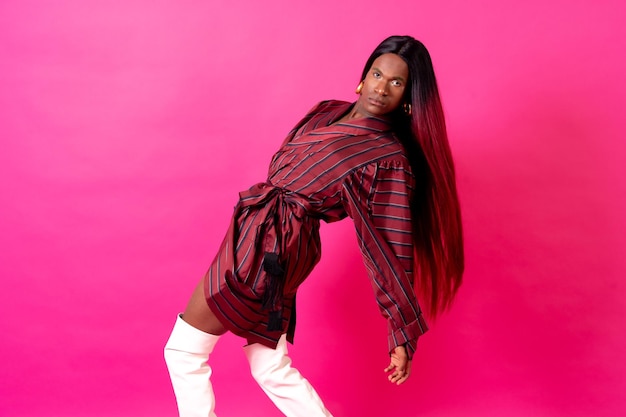 Black ethnic man in a studio LGTBI concept red kimono and white high heels on a pink background