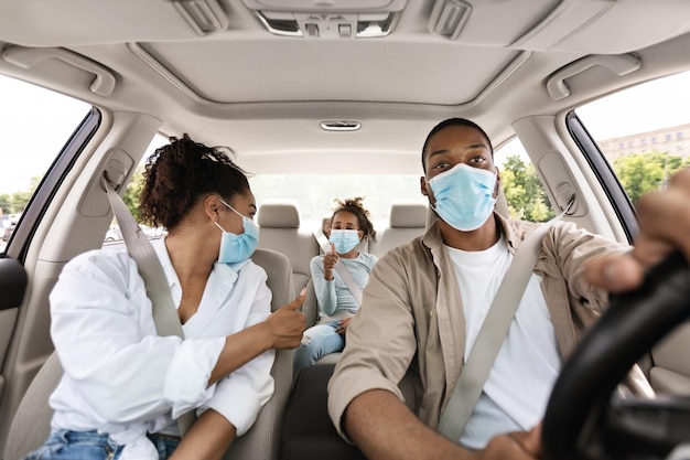 Black family riding car wearing face masks gesturing thumbs up