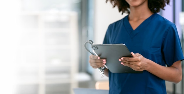 Black female nurse or doctor holding stethoscope and digital tablet standing in hospital office copy space