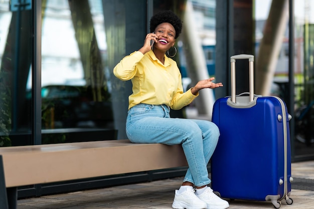 Black Female Traveler Talking On Cellphone Sitting In Urban Area