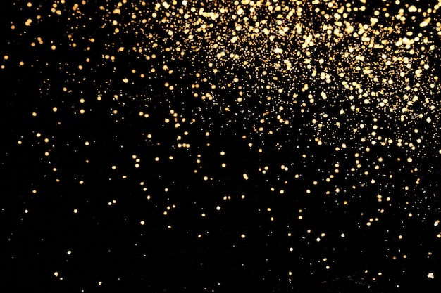 Black festive background. Abstract scattering of gold sparkles on black. Holiday backdrop, selective focus.