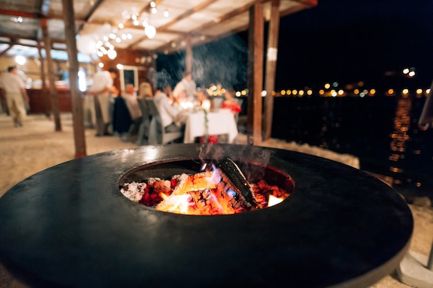 Black flat grill round shape with a hole with a fire in the center in the background of the people