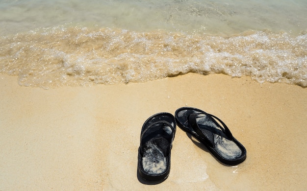 Black flip flops sandal on sand beach and  sea wave.Summer holiday sunny my day off concep