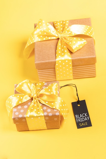 Black friday sale concept with two wrapped gift boxes and black tag on yellow background