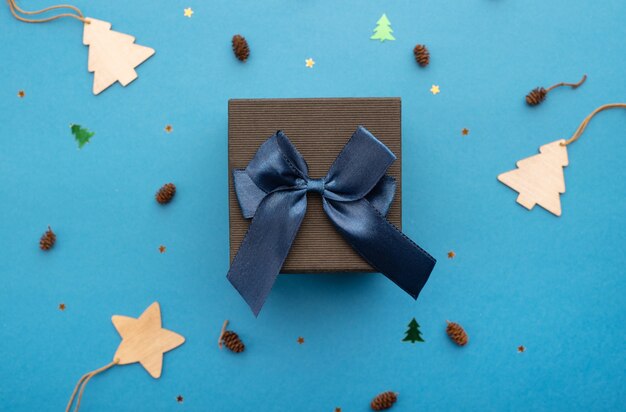 Black gift box with a blue ribbon on a light blue background with stars cones and Christmas trees