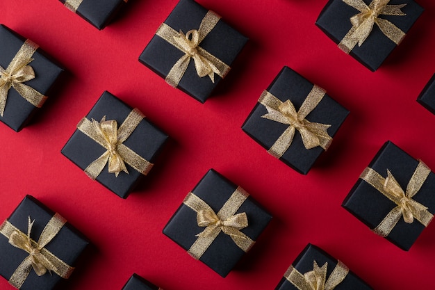 Black gift box with golden ribbons on red paper surface, pattern, texture, isolated, top view, flat lay