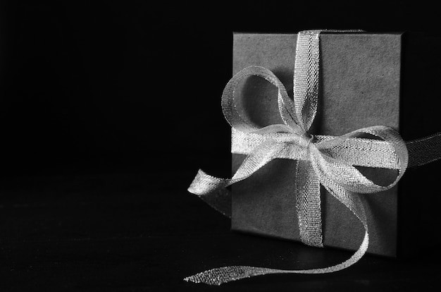 Black gift box with silver ribbon bow on black background.