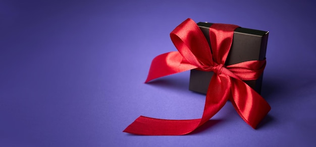 Black gift with red ribbon on purple background Valentines day Birthday or Holidays concept Copy space