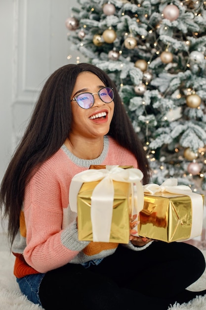 Black girl in eyeglasses near Christmas tree holding a gift